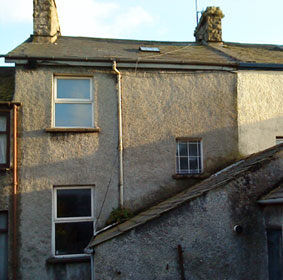 Rear view of cement rendered townhouse with many signs of damp